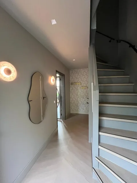 Entree met houten trap, golvende spiegel en een wand met geometrisch behang en kapstokhaken