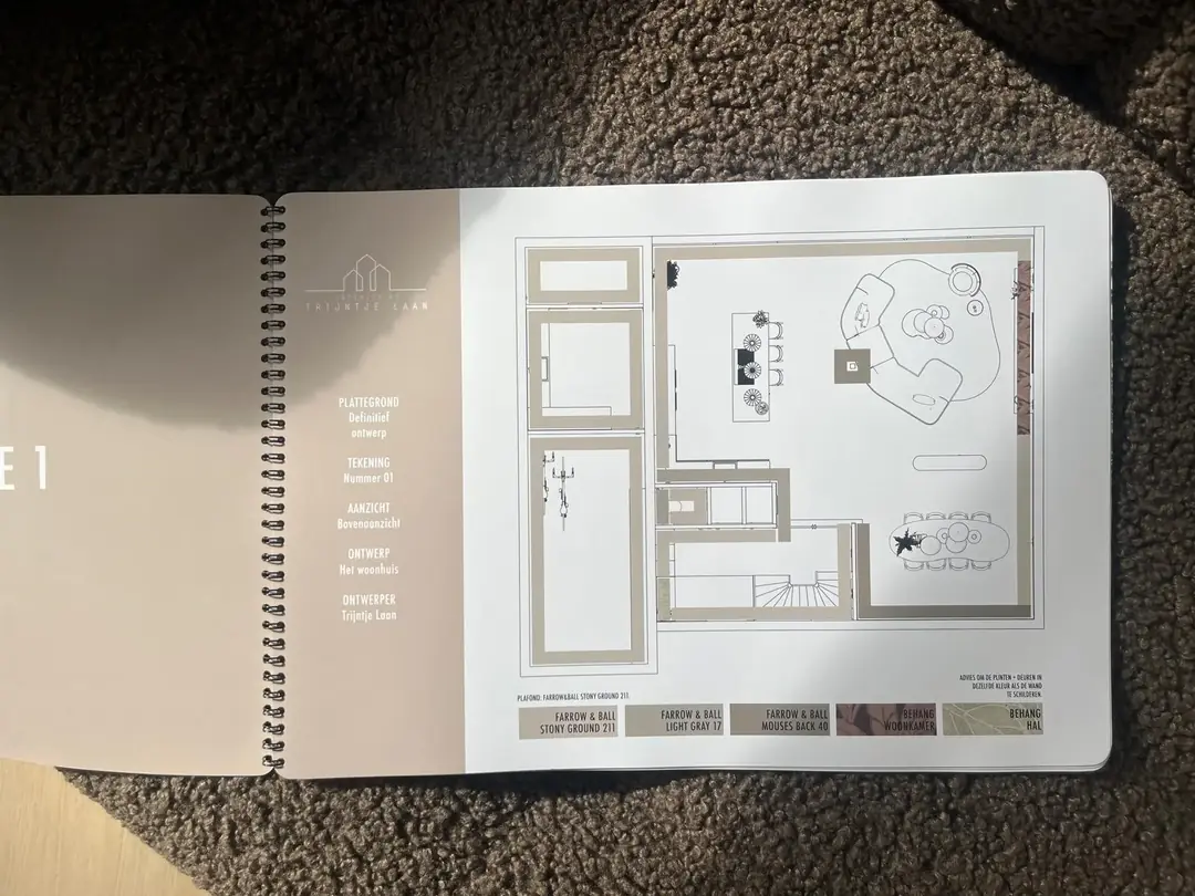 Ontwerpboek open op een ingekleurde plattegrond met kleuradvies voor verf, behang en plafond