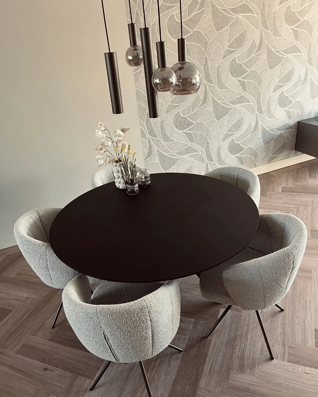 Zwarte ronde eettafel met bouclé stoelen onder rookglazen hanglampen